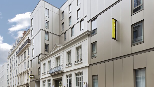 Un hôtel à plusieurs étages, doté d’une façade classique, de grandes fenêtres et d’une enseigne jaune indiquant qu’il s’agit d’un hôtel.
