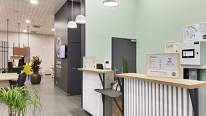 Un hall d’hôtel moderne, doté d’un comptoir d’accueil, d’une grande plante en pot et d’un téléviseur fixé au mur.
