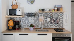 A kitchen with a microwave, coffee maker, sink, and stove. There is a basket on the microwave, a coffee pot, and a shelf with jars and a basket. - Quartino Napoletano (Naples)