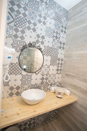 A bathroom with a wooden vanity, a white sink, a mirror, and patterned tiles. - Quartino Napoletano (Naples)