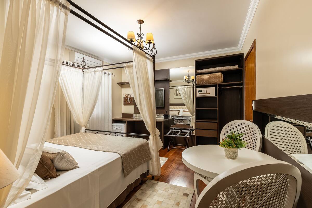 A bedroom with a canopy bed, a desk, a chair, and a small table with a plant.
