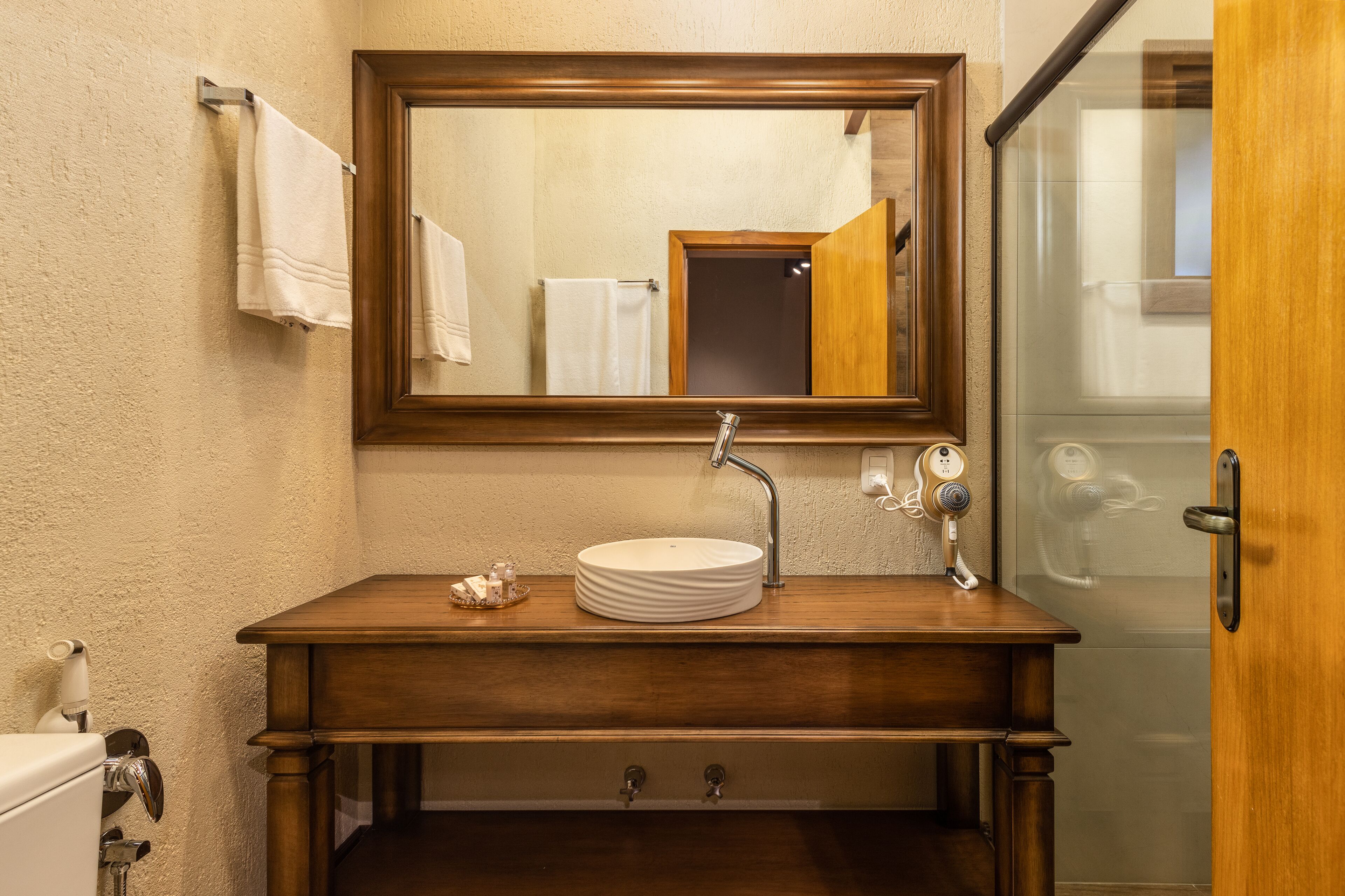 A bathroom with a wooden vanity, a round sink, a mirror, and a towel rack.