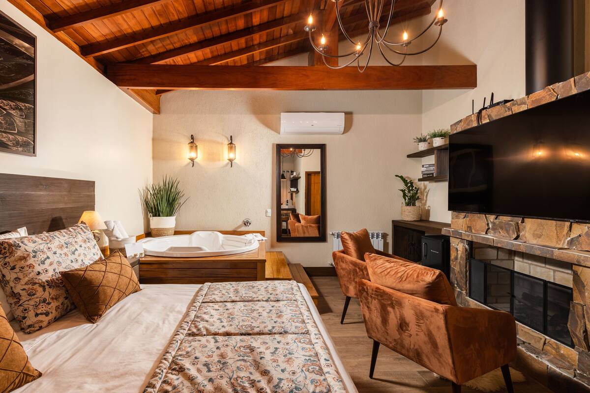 A bedroom with a large bed, a sitting area with a fireplace, and a television.