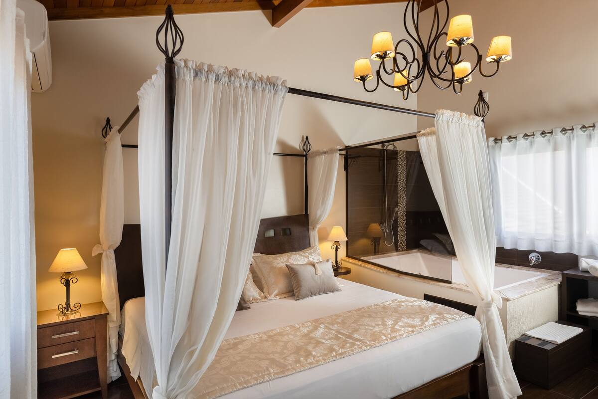 A four-poster bed with white drapes, a bedside table with a lamp, and a large mirror above the bed.