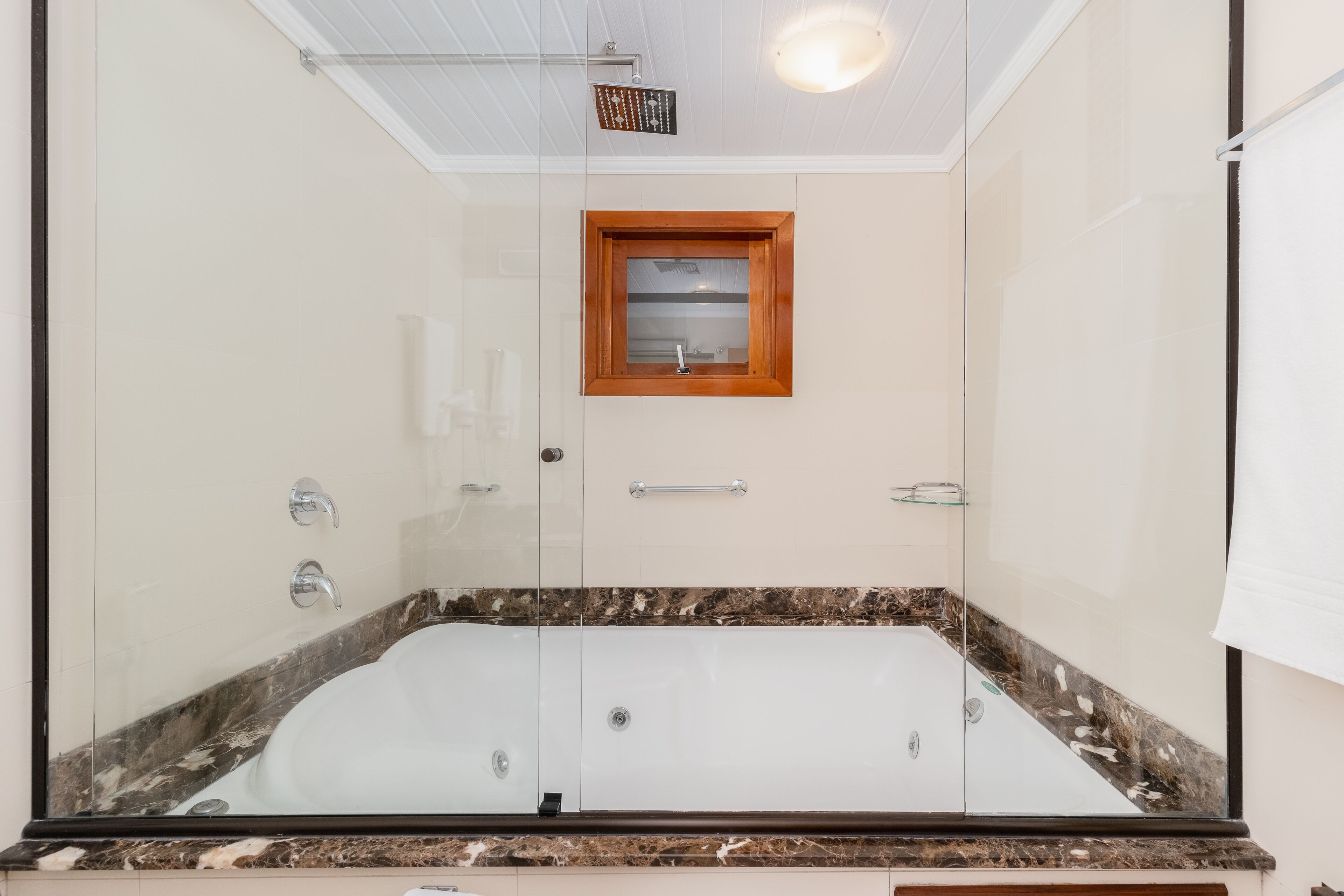 A modern bathroom with a glass-enclosed bathtub, a wooden-framed window, and a marble countertop.