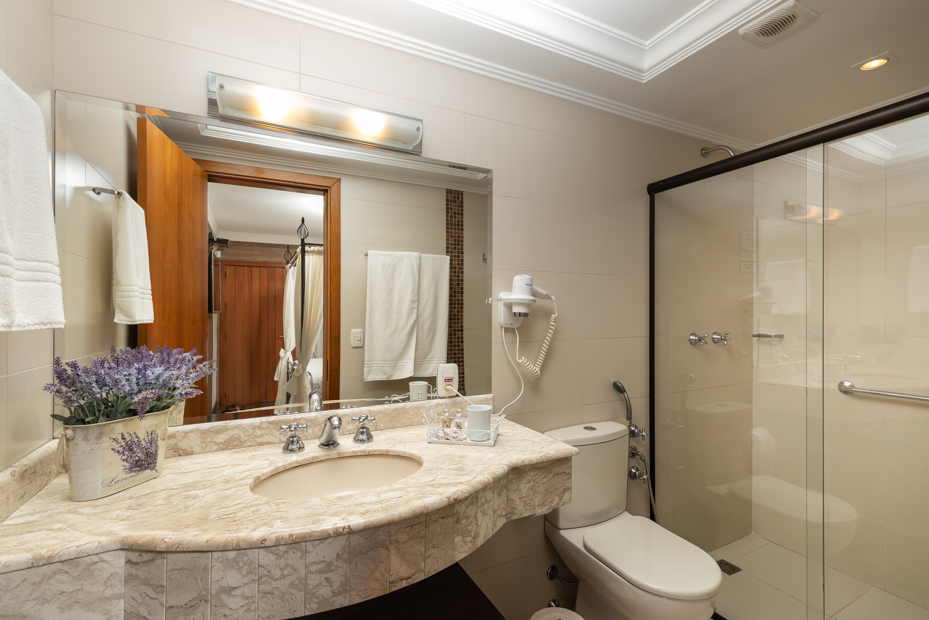 A modern bathroom with a marble sink, a toilet, a glass shower enclosure, and a mirror with a towel rack.