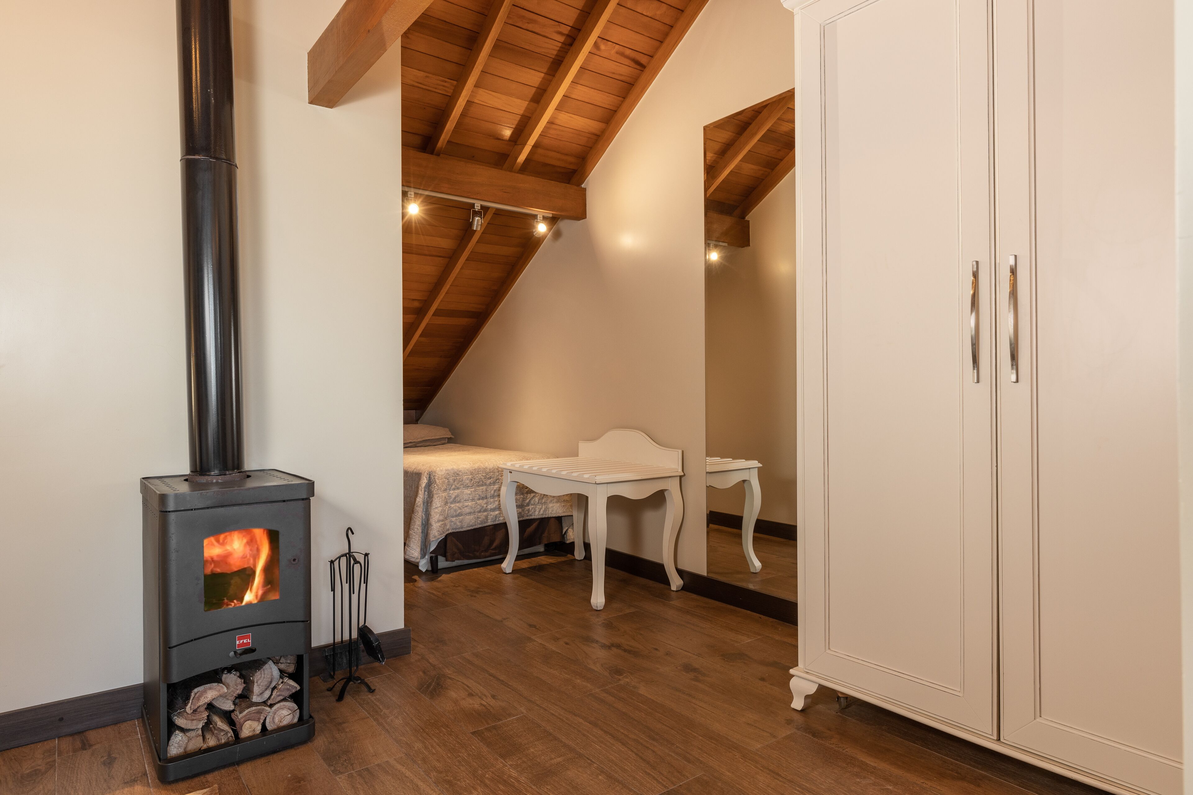 A room with a wood-burning stove, a bed, a small table, and a wardrobe.