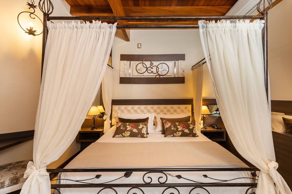 A four-poster canopy bed with a tufted headboard, two bedside tables with lamps, and floral-patterned pillows.