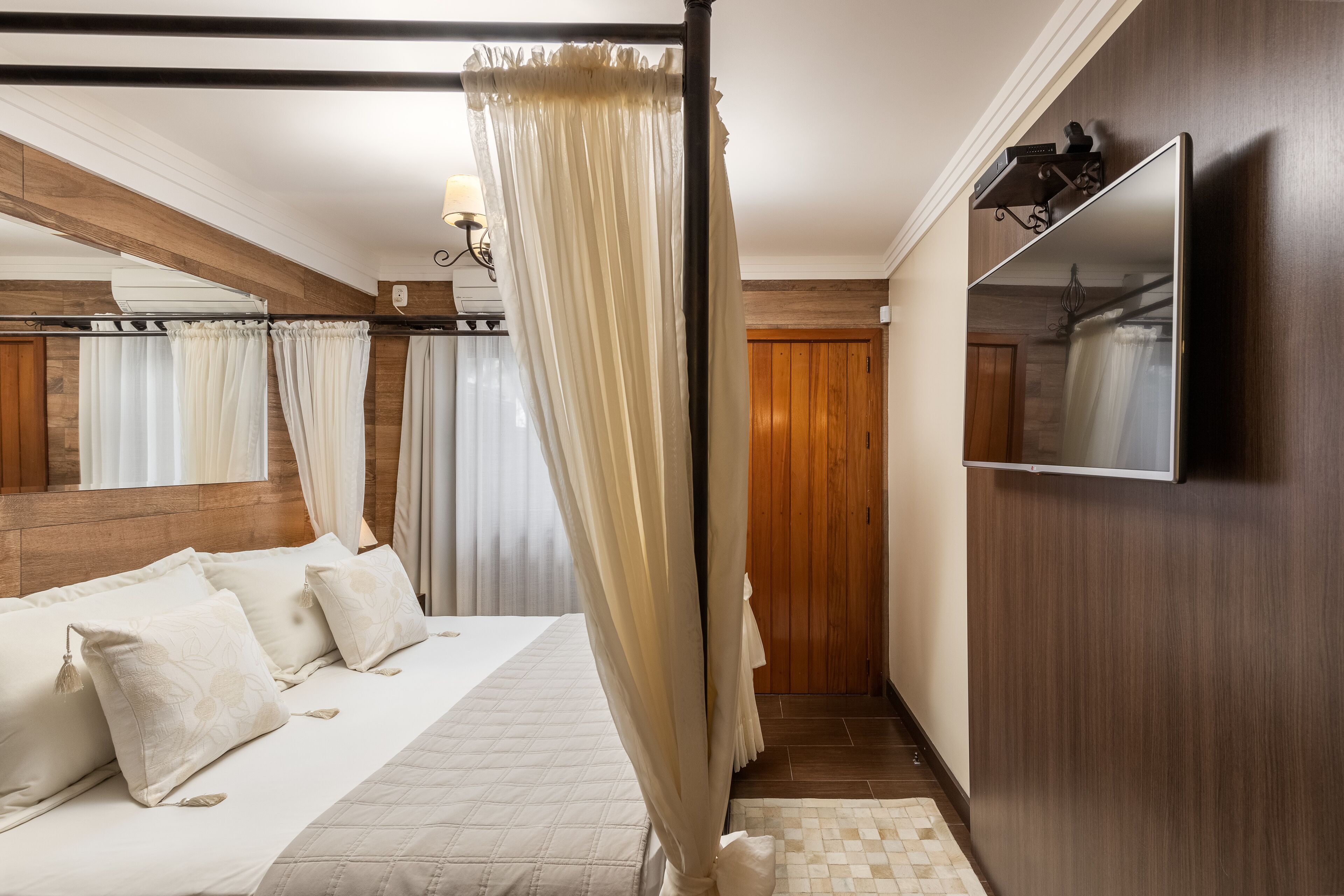 A bedroom with a bed, curtains, a TV, and wooden paneling.