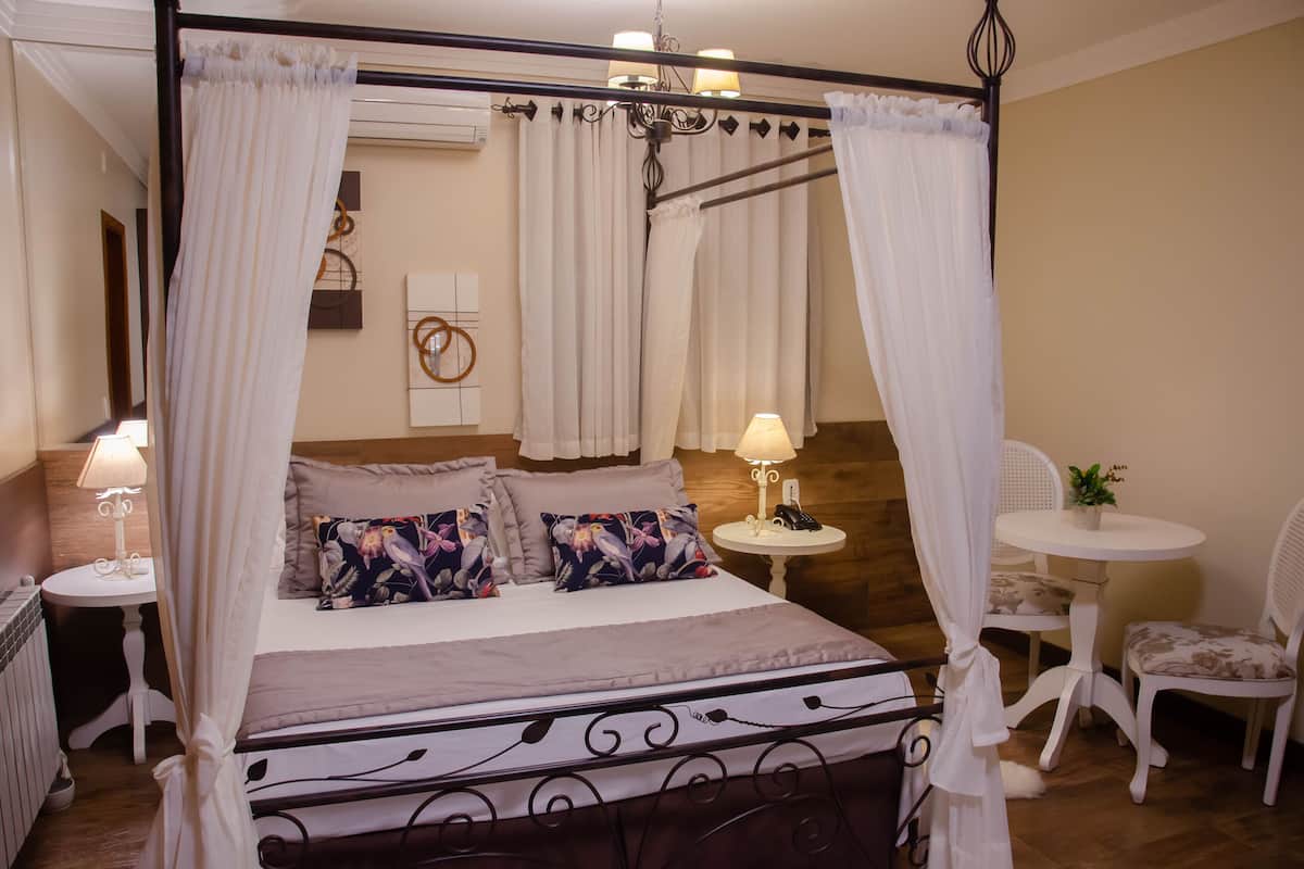 A four-poster bed with a canopy, a bedside table with a lamp, a small round table with a lamp, and two chairs.