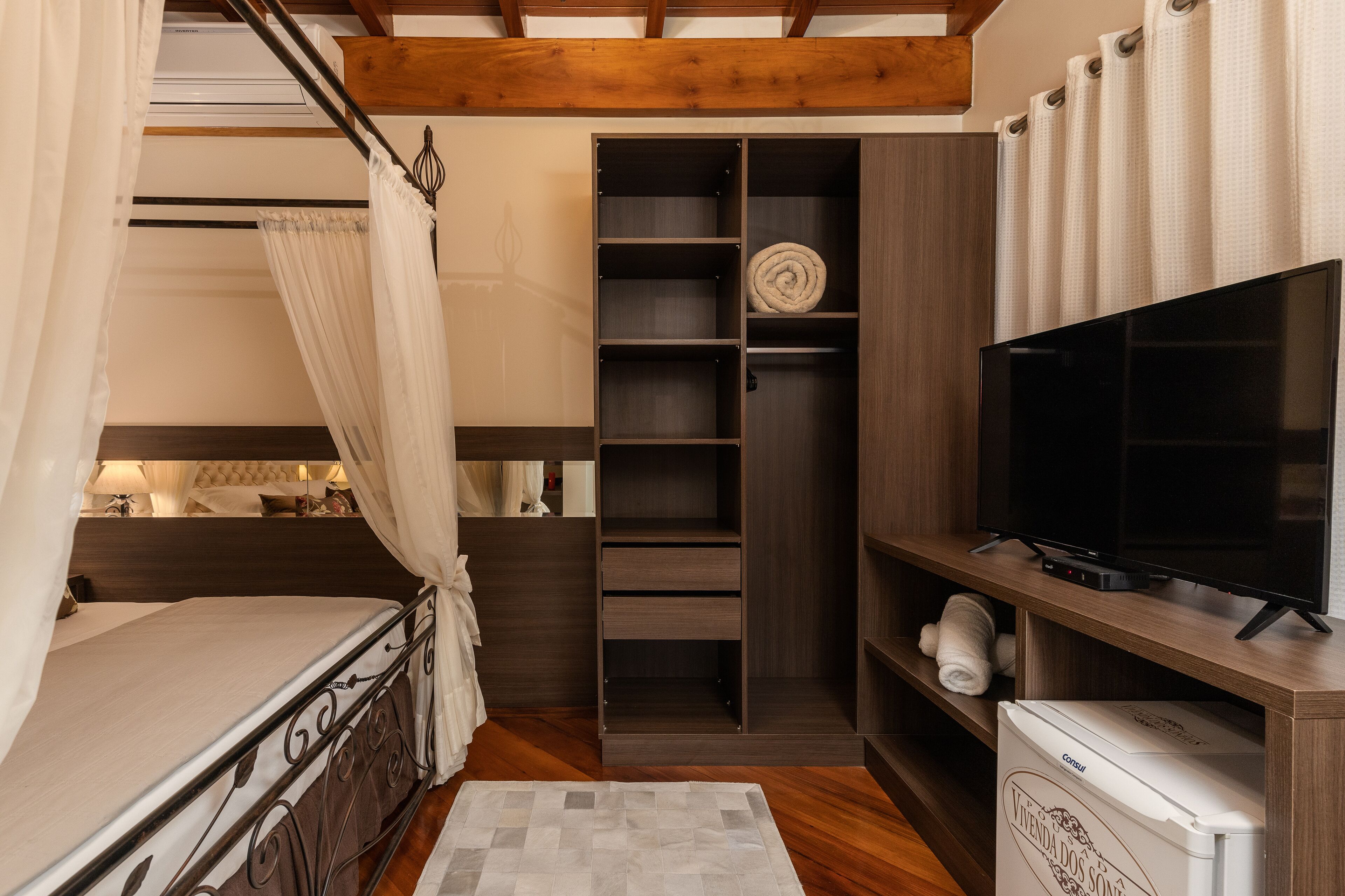A bedroom with a bed, a TV, a wardrobe, and a small white appliance.