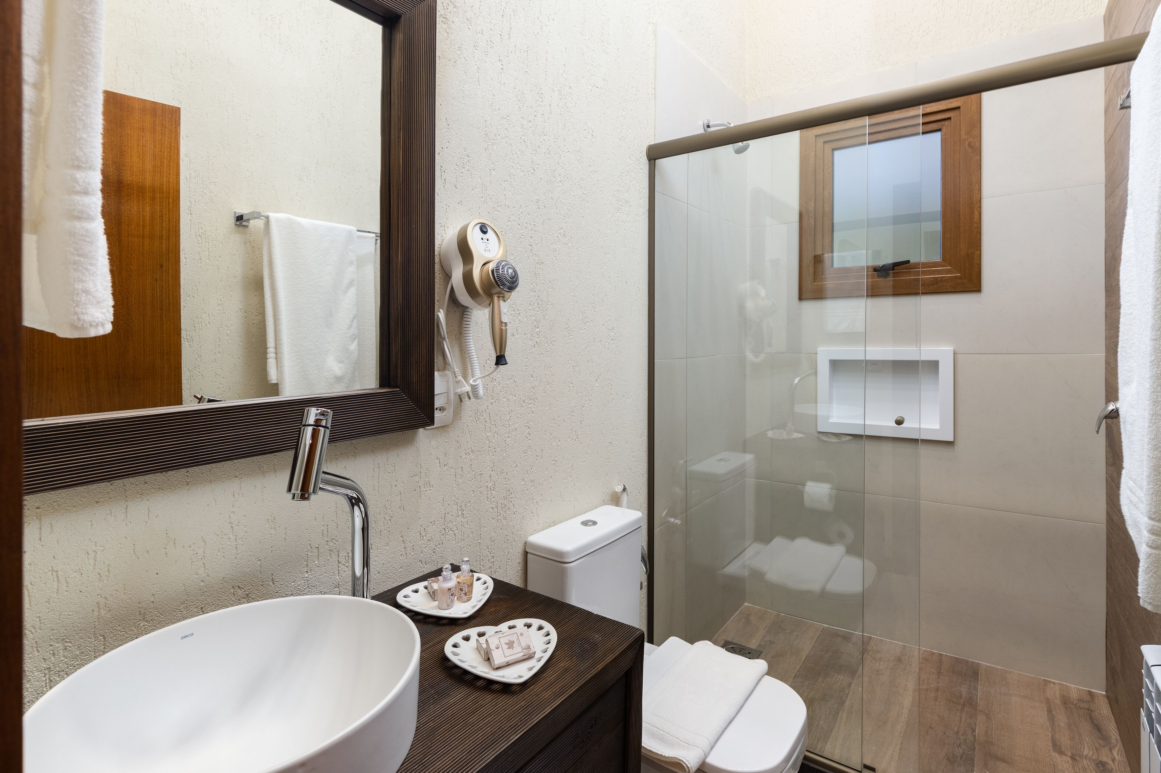 Un baño moderno con un lavamanos grande, un espejo, un secador de pelo, una cabina de ducha de vidrio y un inodoro.