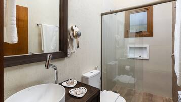 Un baño moderno con un lavamanos grande, un espejo, un secador de pelo, una cabina de ducha de vidrio y un inodoro.