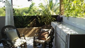 A patio area with wicker chairs and a small table, surrounded by lush greenery and a white tiled wall. - Le Creole Hideaway (Jacmel)