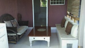 A room with a wooden table, a white sofa, and a wicker chair. - Le Creole Hideaway (Jacmel)