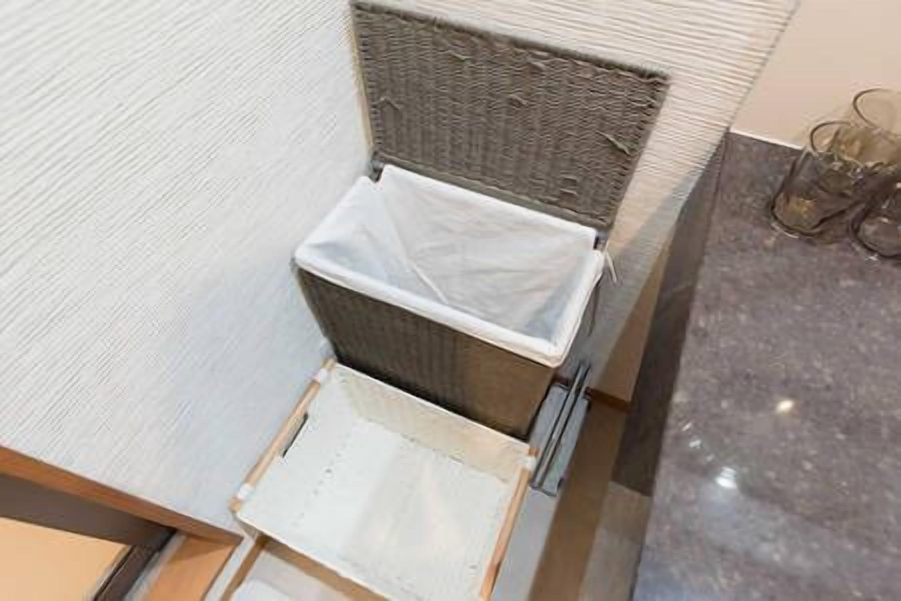 A small, enclosed trash bin with a lid, located on a wooden surface next to a wicker chair.