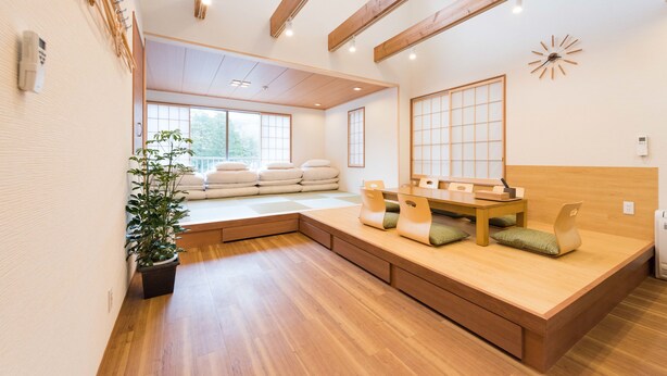 A room with a wooden floor, a built-in bench with cushions, a small table, and a potted plant. - Guestvilla Hakone Miyanoshita (Hakone)