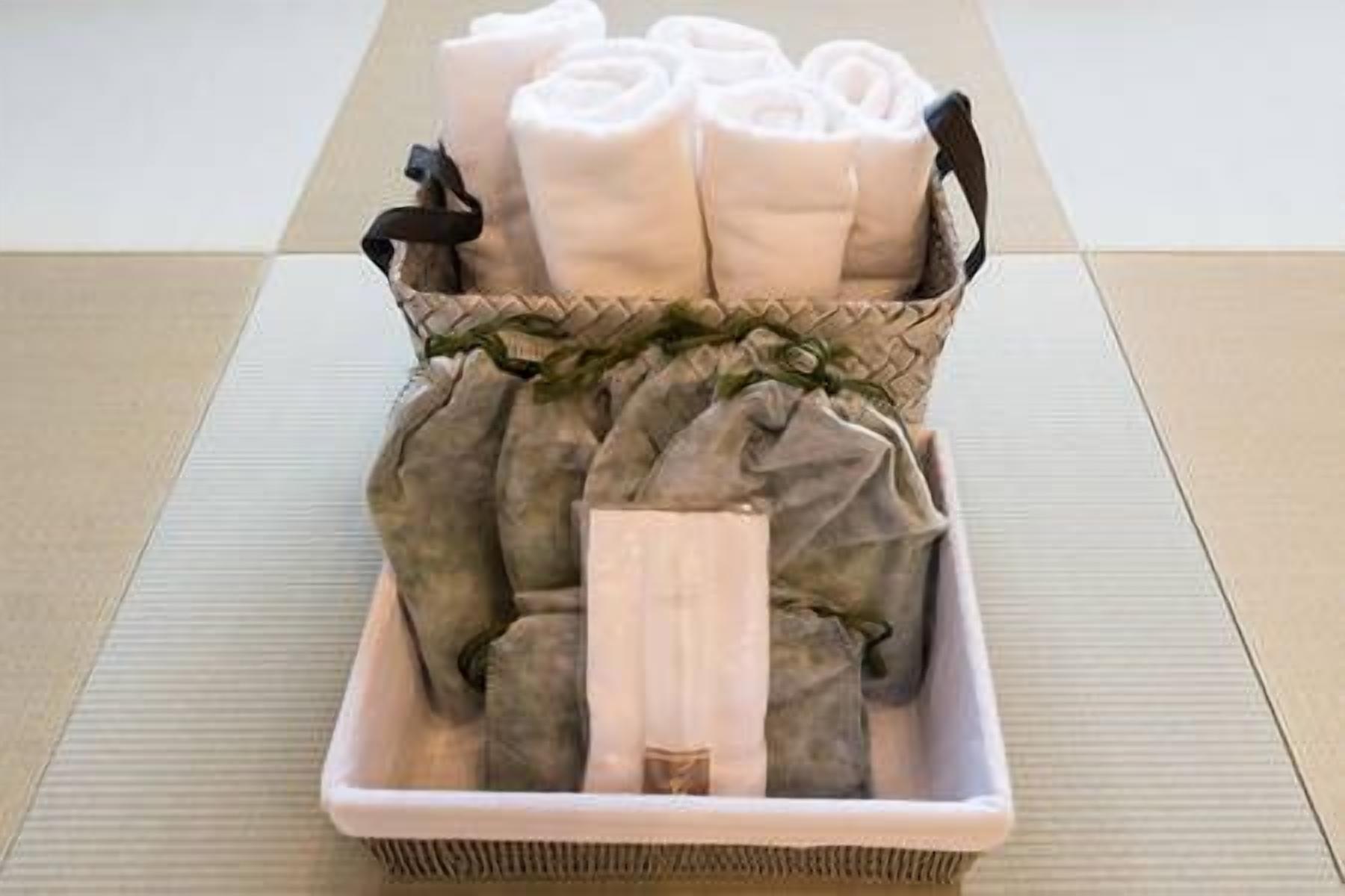 Una cesta con toallas dobladas cuidadosamente y un tapete enrollado sobre un suelo de esteras de tatami.