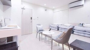 A modern, minimalist room with a white color scheme, featuring a desk with a computer, a chair, a small round table, and a stack of folded towels. - Guestvilla Hakone Miyanoshita (Hakone)