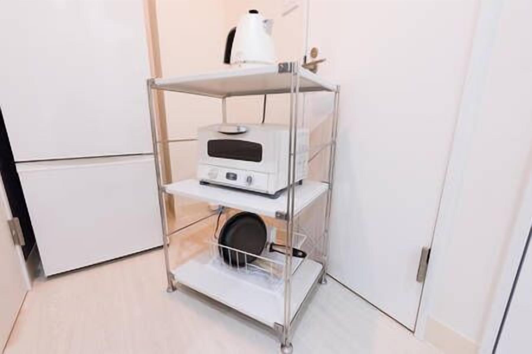Un carrito metálico blanco con una cafetera y un pequeño electrodoméstico, posiblemente un microondas, sobre un suelo de baldosas.