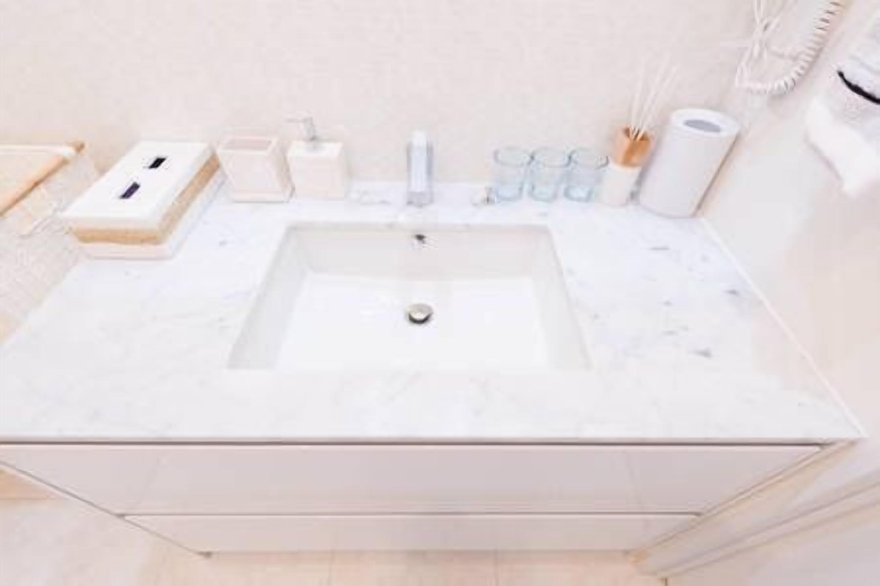 Une salle de bain avec un lavabo en marbre blanc, un distributeur de savon, un porte-brosse à dents et un porte-serviettes.