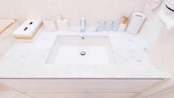 Une salle de bain avec un lavabo en marbre blanc, un distributeur de savon, un porte-brosse à dents et un porte-serviettes.