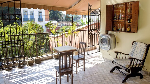 A balcony with a table and chairs, potted plants, and a wooden cabinet with bottles. - Rio Antigo (Rio de Janeiro)