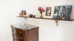 A wooden dresser with drawers, a vase with flowers, and a shelf with books, a framed photo, and a book titled "Amazonia." - Rio Antigo (Rio de Janeiro)