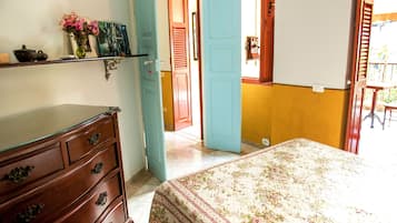 A bedroom with a wooden dresser, a bed with a floral bedspread, and a door leading to another room.