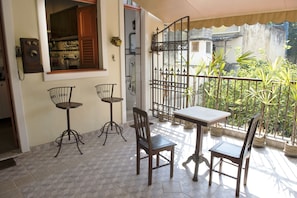 Uma varanda com mesa e cadeiras, um portão de metal e vasos com plantas.