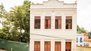 A two-story building with a white facade, multiple windows with wooden shutters, and a balcony. - Rio Antigo (Rio de Janeiro)