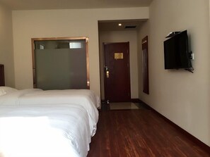 Quarto de hotel com uma cama grande, piso de madeira, televisão presa à parede e uma porta que dá para outro cômodo.