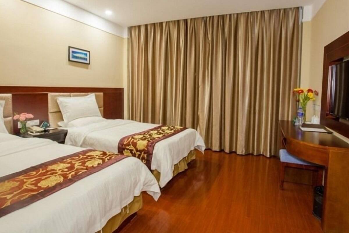 A hotel room with two beds, a desk, and a large window with curtains.