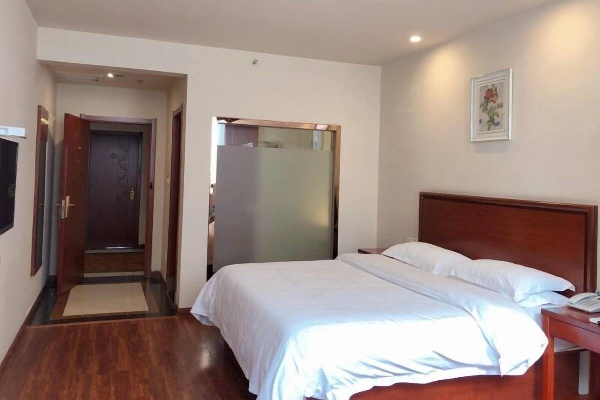 A hotel room with a wooden bed, a bedside table, a door, and a wall-mounted picture.