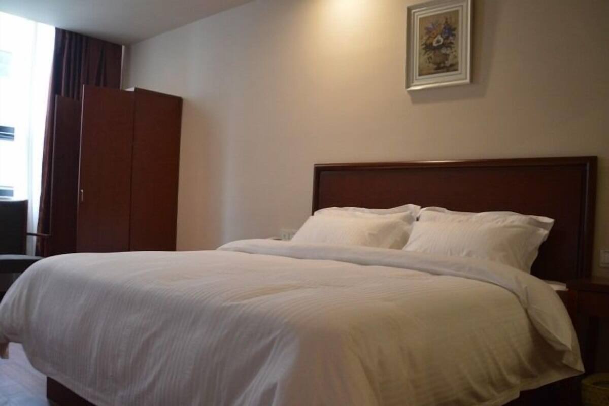 A neatly made bed with white linens in a hotel room.