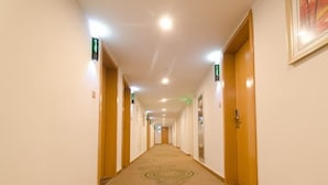A hotel hallway with doors on both sides, carpeted floors, and overhead lighting.