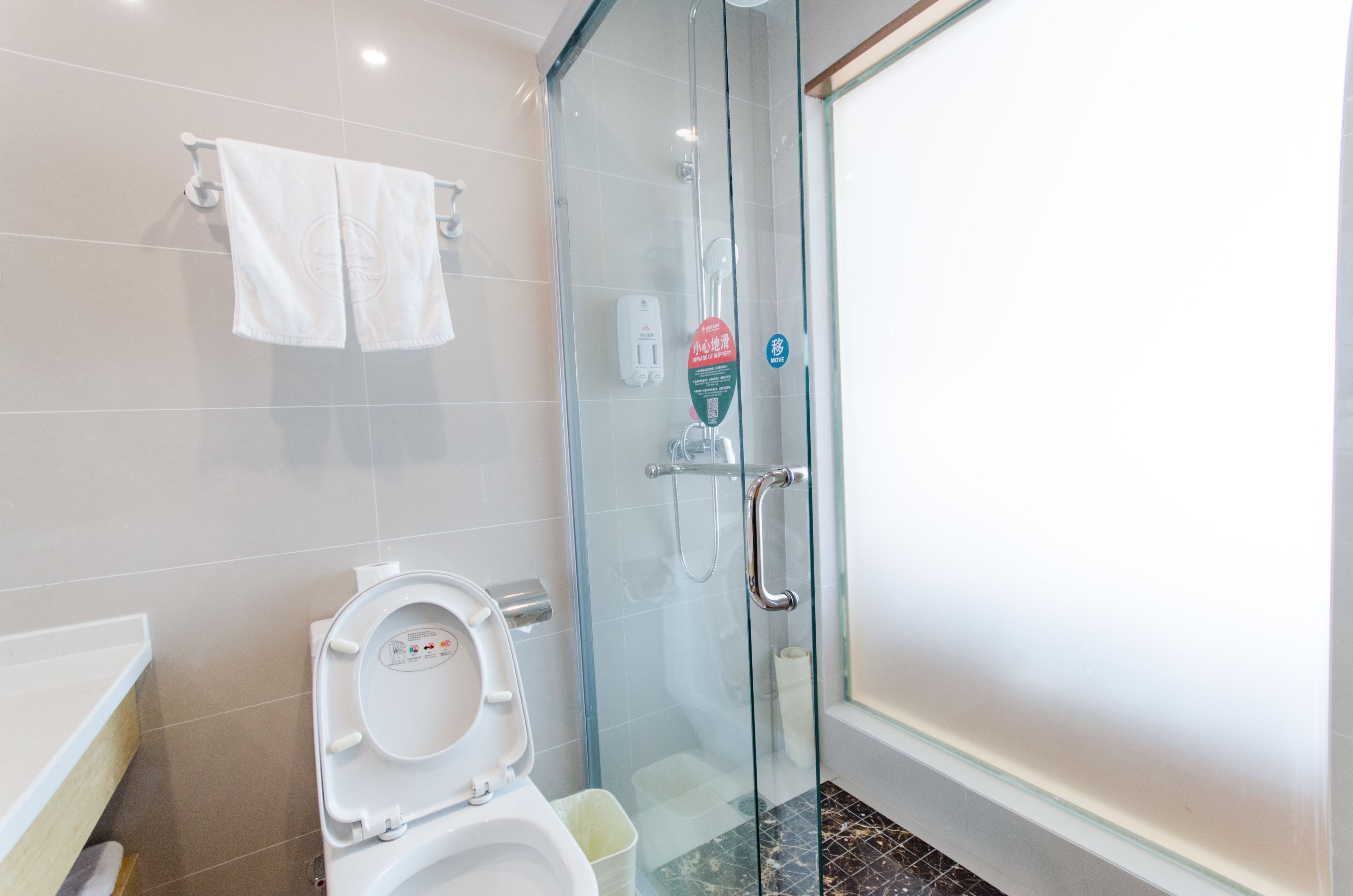 Et moderne badeværelse med et brusebad bag glas, et toilet med kontrolpanel og et hvidt håndklæde på en håndklæderække.