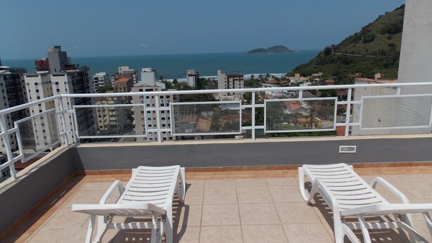 Un balcón con dos sillones blancos, piso de baldosas y vista al mar y edificios.