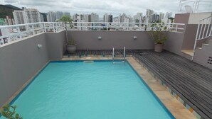 Una piscina en la azotea con terraza de madera y plantas en macetas.