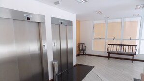 Un área de ascensores moderna con dos ascensores, un banco y una ventana con persianas.