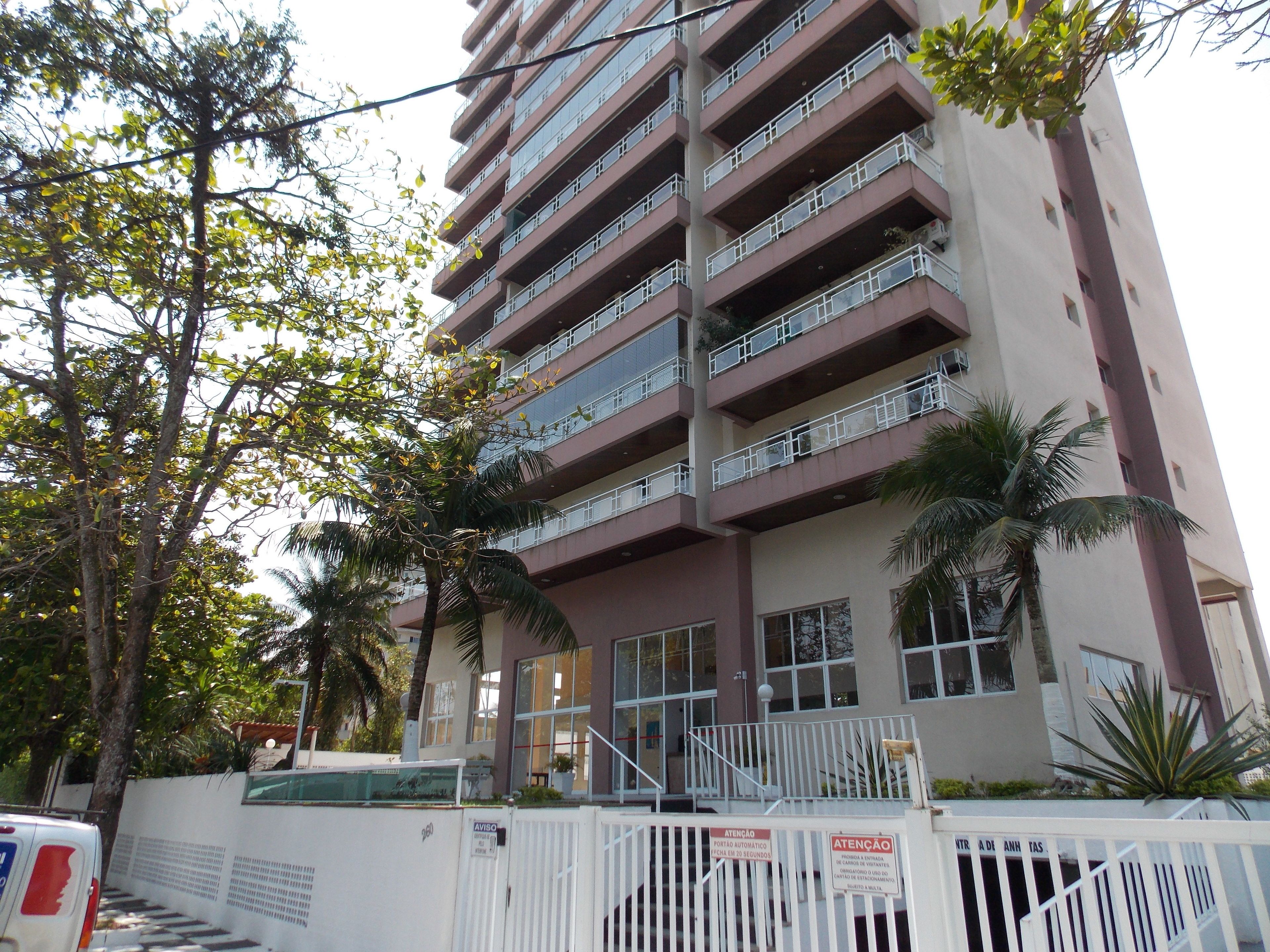Un edificio de varios pisos con balcones, una entrada protegida por una reja y árboles alrededor.