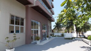 Un edificio de varios pisos con amplias ventanas y balcones, rodeado de macetas con plantas y árboles.