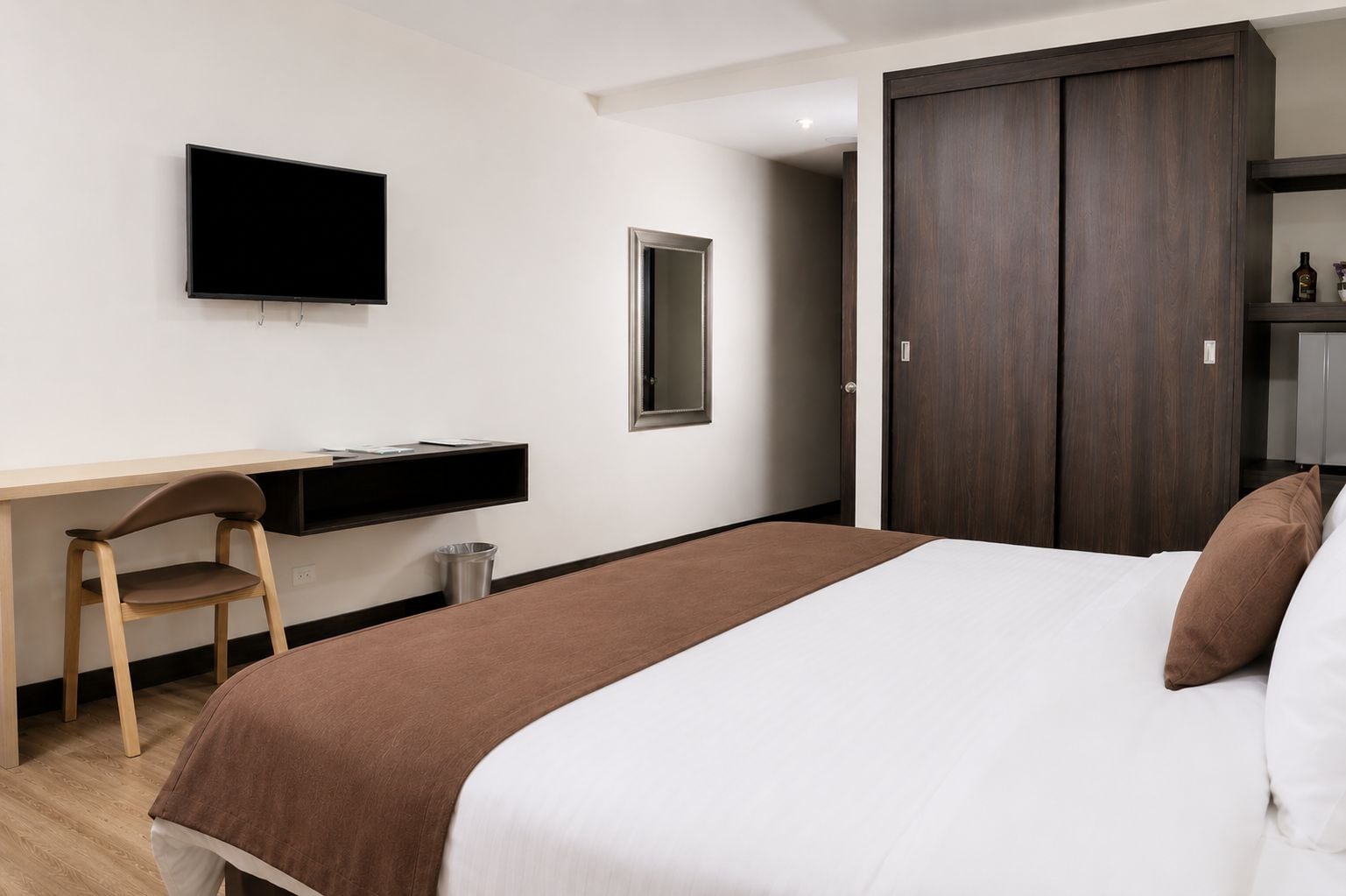A hotel room with a bed, a desk, a chair, a television, a wardrobe, and a mirror.