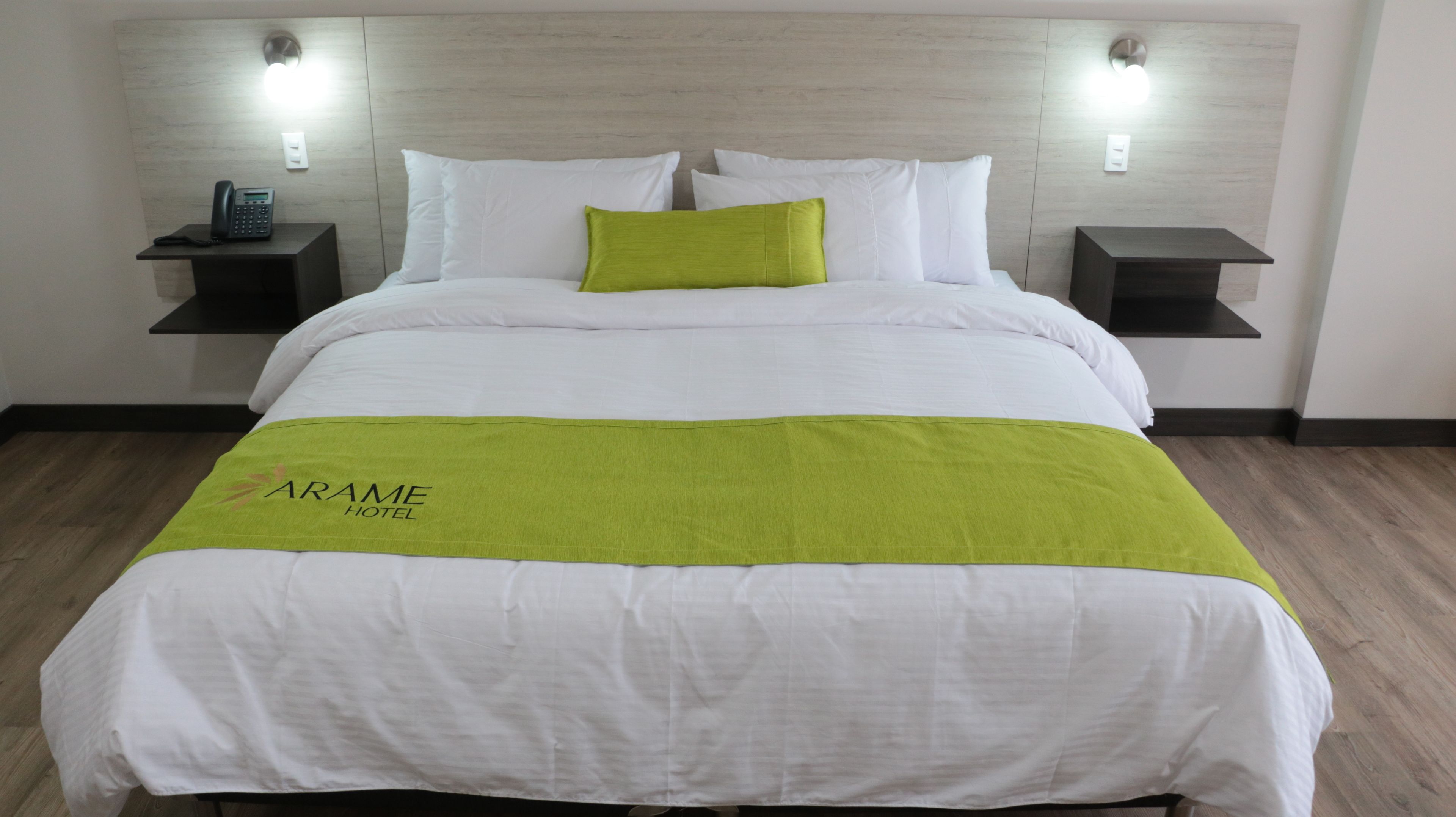 A hotel room with a bed, a green throw, white bedding, two bedside tables, and a phone on one table.