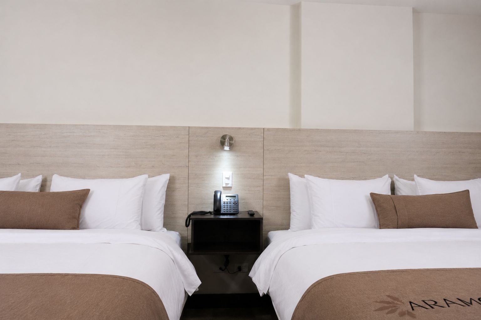 A hotel room with two beds, a bedside telephone, and a wall-mounted light fixture.
