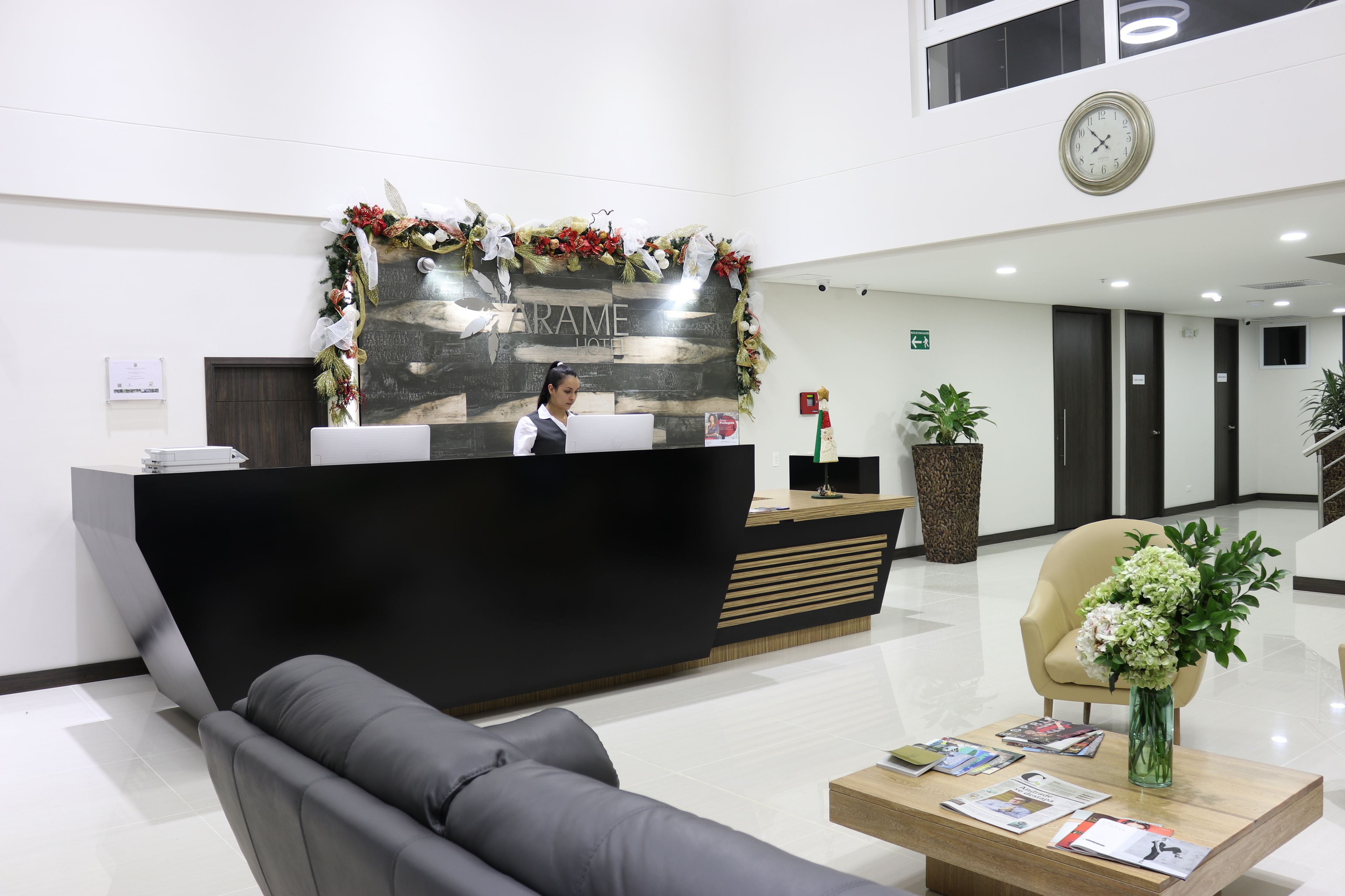 A hotel reception area with a modern desk, a sofa, a coffee table with magazines, and a clock on the wall.