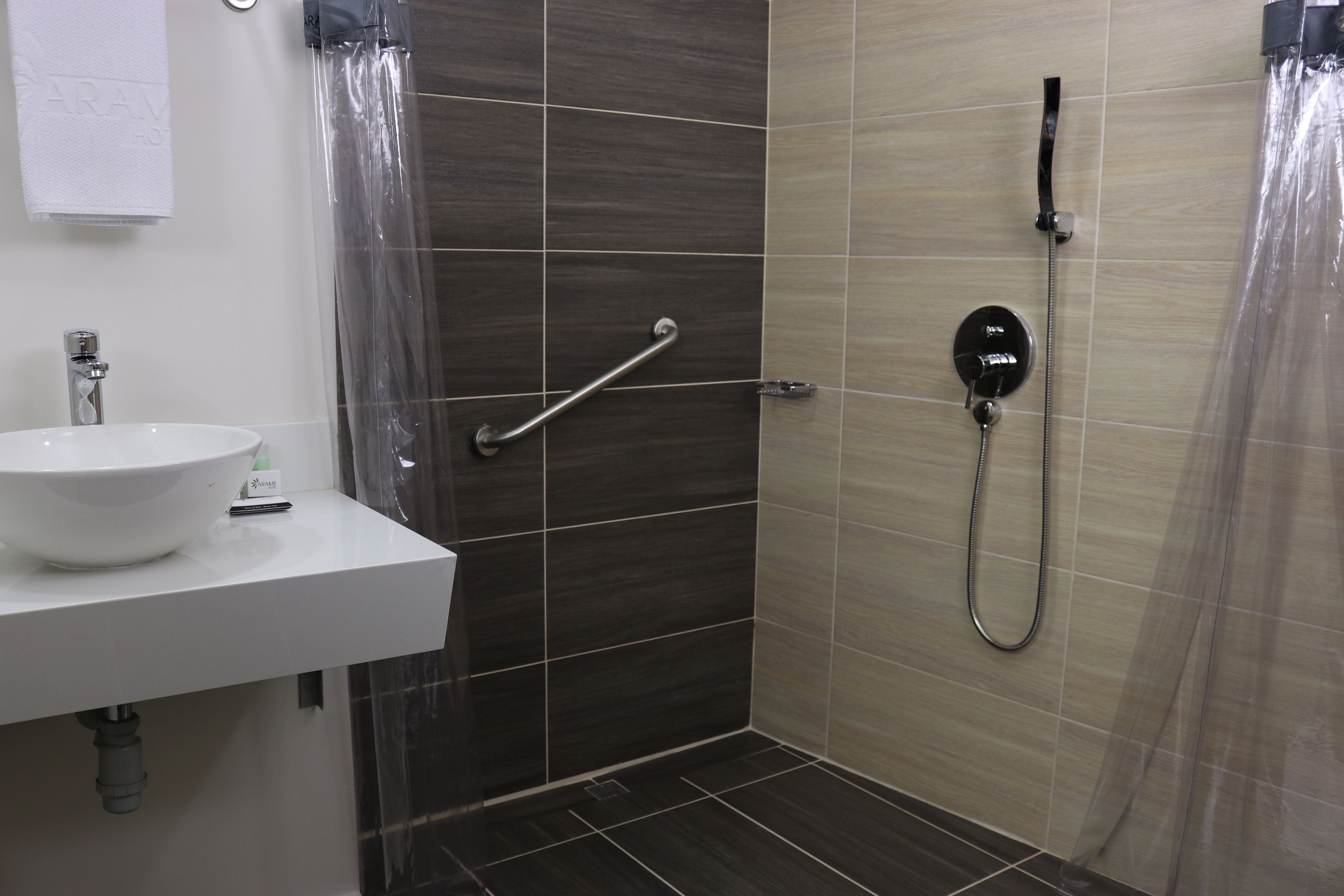 A bathroom with a white sink, a shower with a handheld showerhead, and a grab bar.