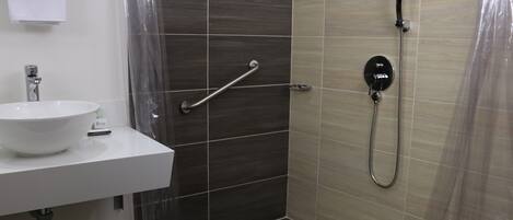 A bathroom with a white sink, a shower with a handheld showerhead, and a grab bar.