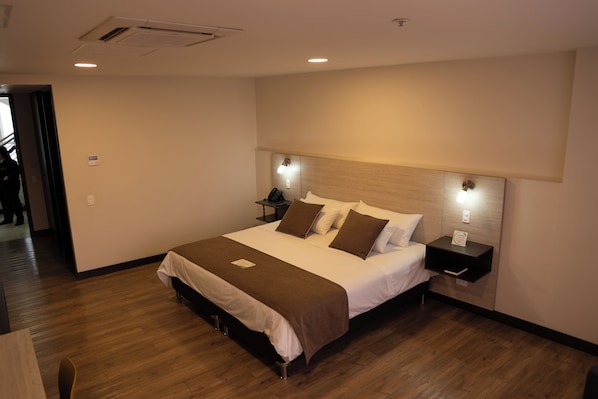Una habitación de hotel con una cama grande, mesitas de noche, un teléfono y una lámpara en la pared.