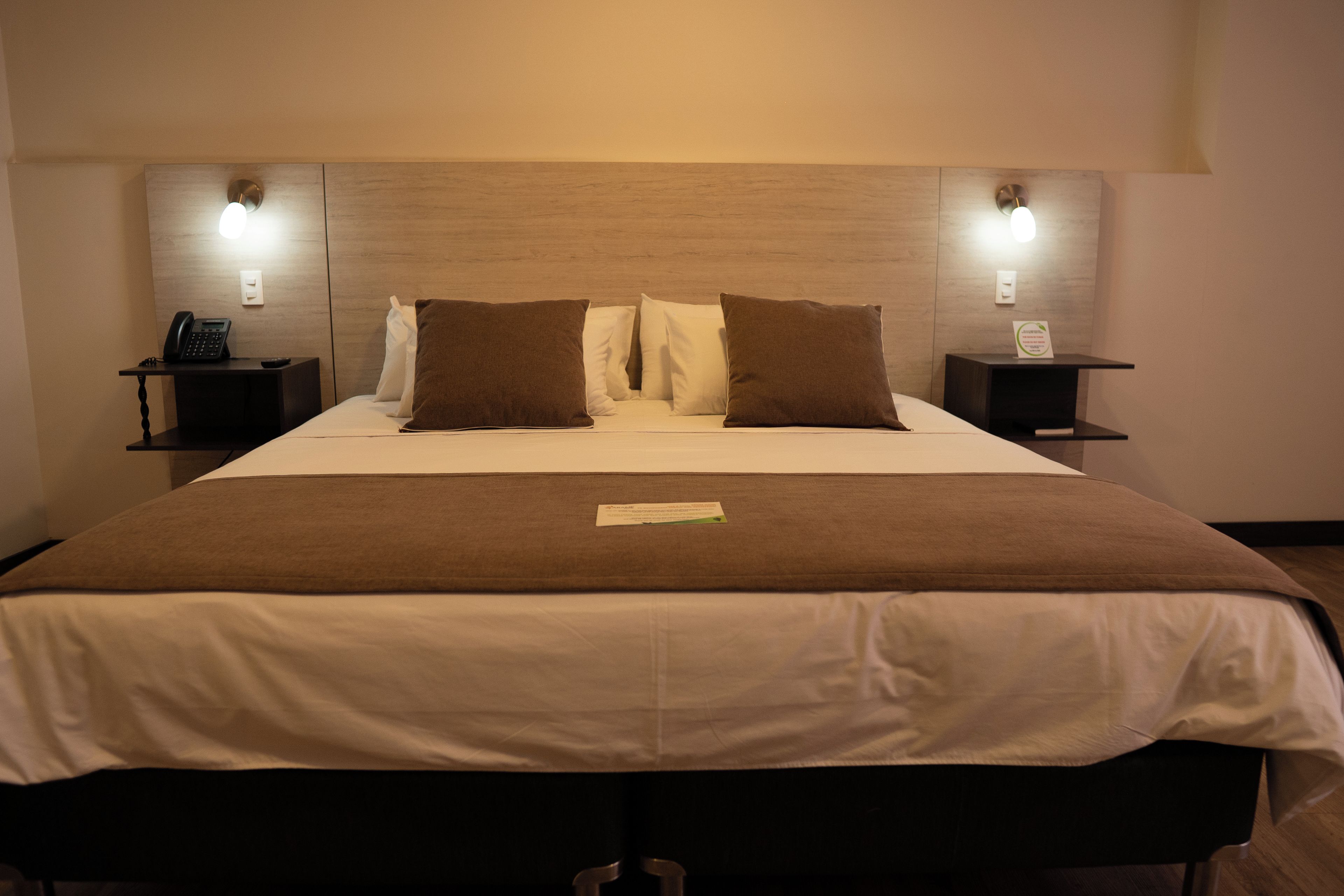 Une chambre d’hôtel avec un grand lit, deux tables de chevet, un téléphone et deux lampes fixées au mur.